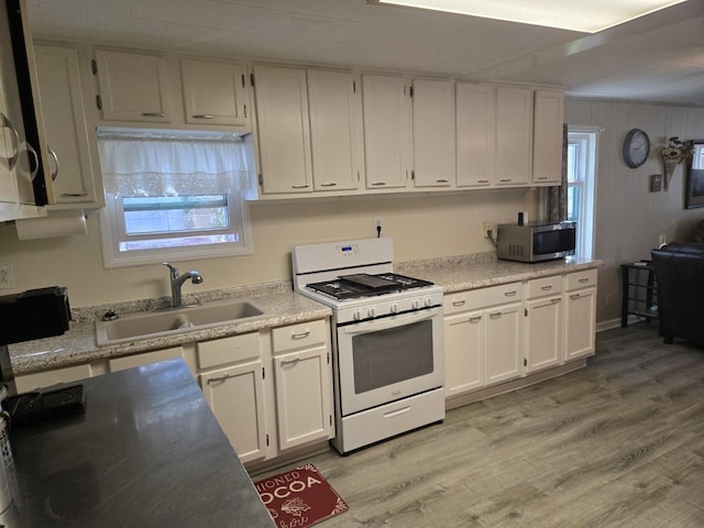 kitchen featuring light wood-style flooring, a sink, white cabinetry, stainless steel microwave, and white gas range