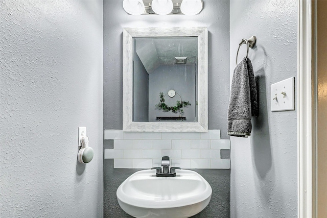 bathroom with decorative backsplash, a textured wall, and a sink