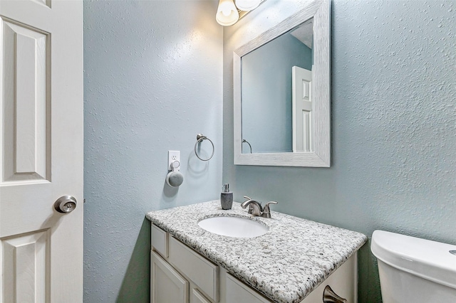 bathroom featuring toilet, vanity, and a textured wall