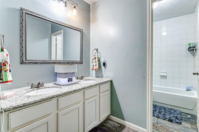 full bathroom featuring a sink, baseboards, wood finished floors, and double vanity