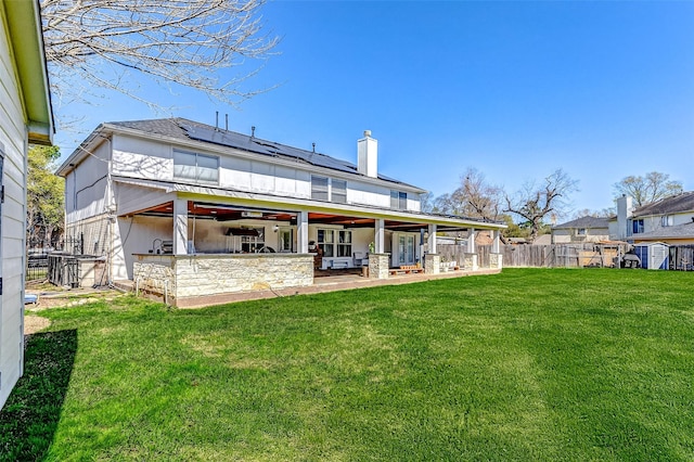 back of house featuring a lawn, fence, solar panels, a chimney, and a patio area