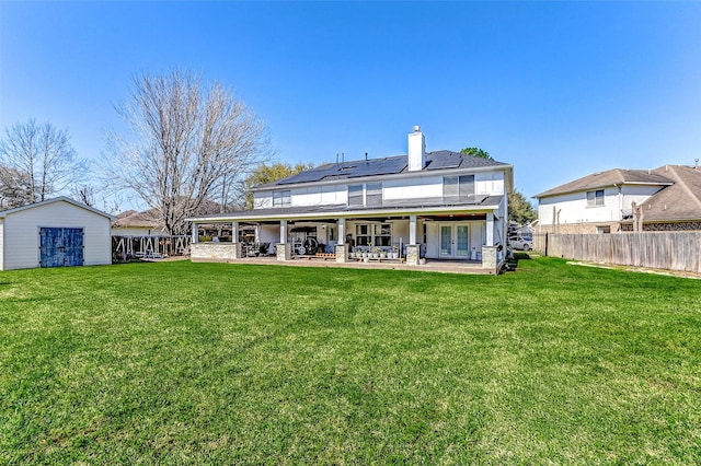 rear view of property featuring a lawn, a patio, a fenced backyard, french doors, and solar panels