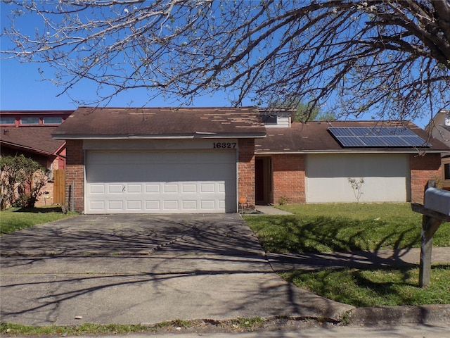 view of front of house with driveway, an attached garage, a shingled roof, brick siding, and solar panels