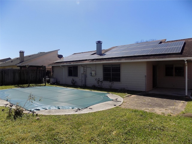 back of property with roof mounted solar panels, fence, a yard, a fenced in pool, and a patio area