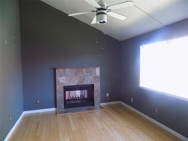 unfurnished living room featuring wood finished floors, baseboards, ceiling fan, a tile fireplace, and vaulted ceiling