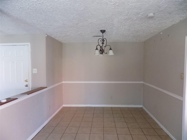 unfurnished dining area featuring visible vents, a textured ceiling, an inviting chandelier, light tile patterned floors, and baseboards