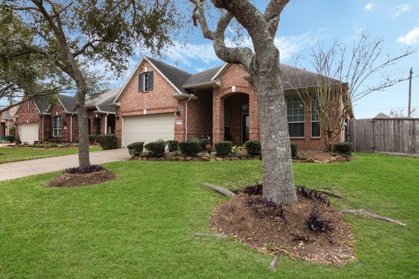 view of front of home with brick siding, concrete driveway, a front lawn, and fence