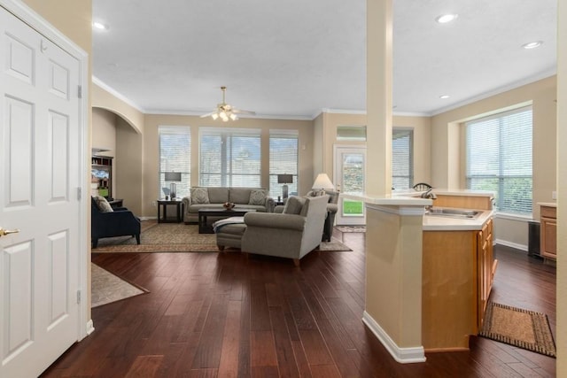 living area featuring a ceiling fan, dark wood-style floors, baseboards, arched walkways, and crown molding