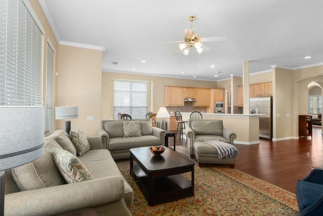 living room featuring dark wood finished floors, crown molding, a ceiling fan, and arched walkways