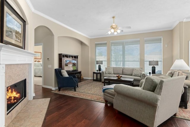 living area with baseboards, ceiling fan, ornamental molding, a fireplace, and hardwood / wood-style flooring