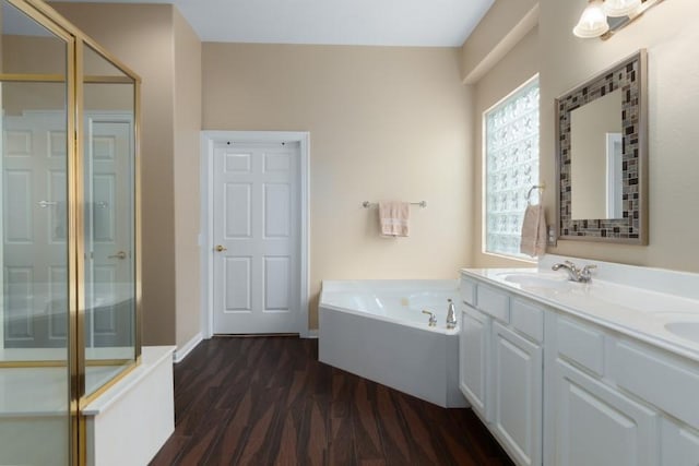 full bath featuring a garden tub, a sink, wood finished floors, double vanity, and baseboards