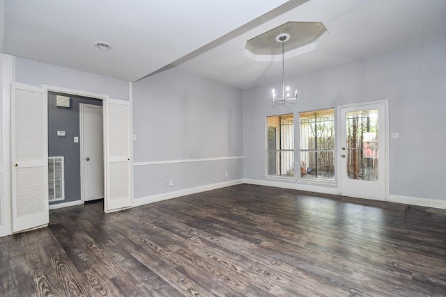 empty room with an inviting chandelier, wood finished floors, baseboards, and visible vents