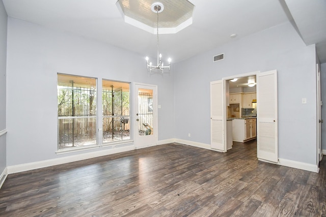 empty room featuring dark wood-style floors, baseboards, a raised ceiling, and an inviting chandelier