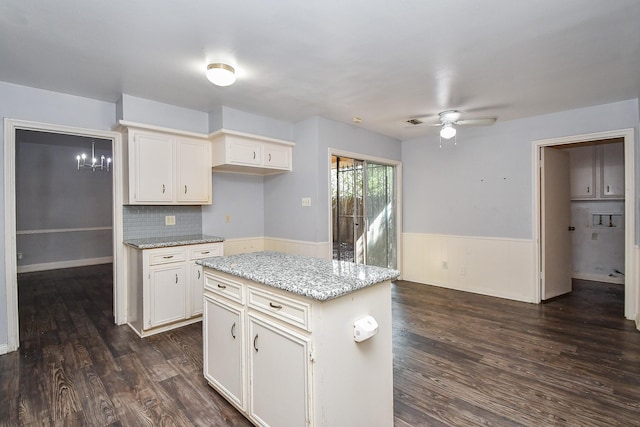 kitchen with light stone counters, dark wood-style floors, white cabinets, wainscoting, and ceiling fan with notable chandelier