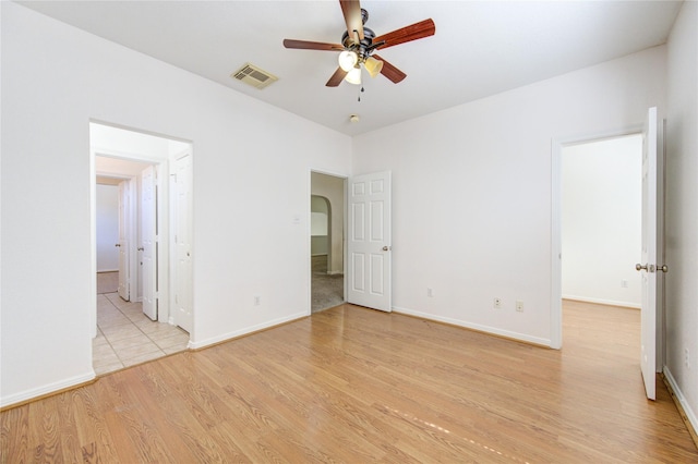 empty room with visible vents, light wood-style flooring, a ceiling fan, arched walkways, and baseboards