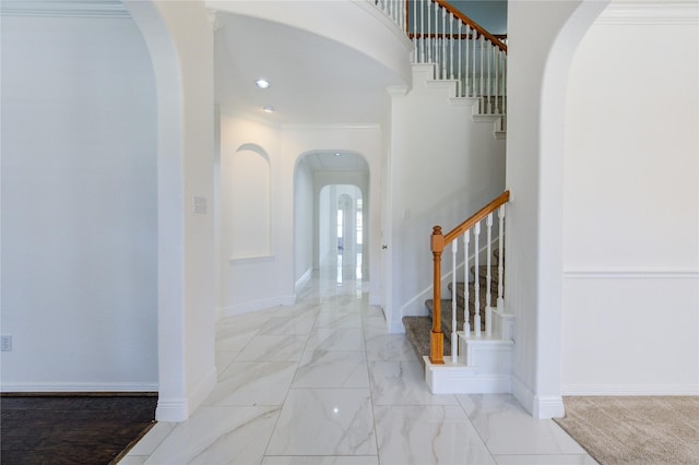 entryway with marble finish floor, stairway, arched walkways, crown molding, and baseboards