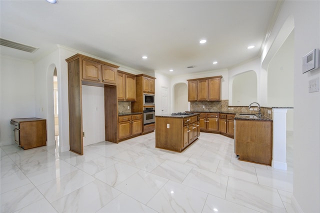 kitchen featuring dark stone counters, arched walkways, a sink, stainless steel appliances, and brown cabinets