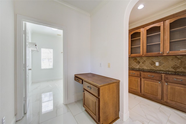 kitchen featuring brown cabinets, glass insert cabinets, marble finish floor, crown molding, and tasteful backsplash