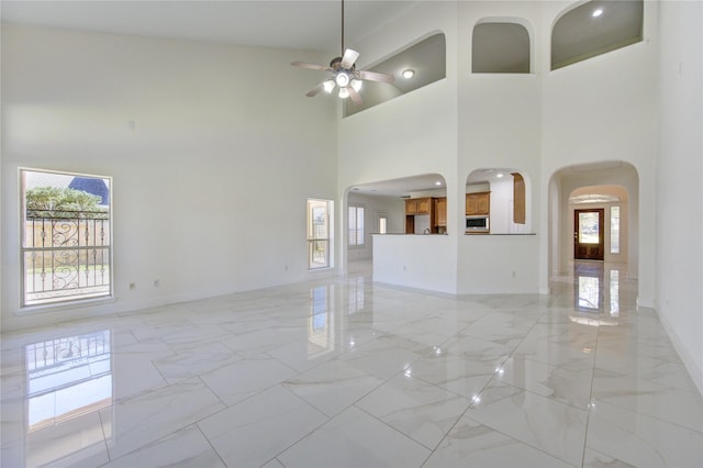 spare room with arched walkways, marble finish floor, baseboards, and ceiling fan