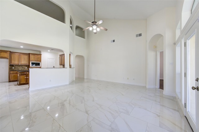 unfurnished living room featuring visible vents, marble finish floor, arched walkways, baseboards, and ceiling fan