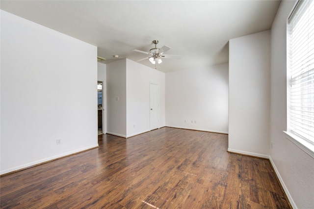 empty room featuring dark wood-type flooring, a ceiling fan, and baseboards