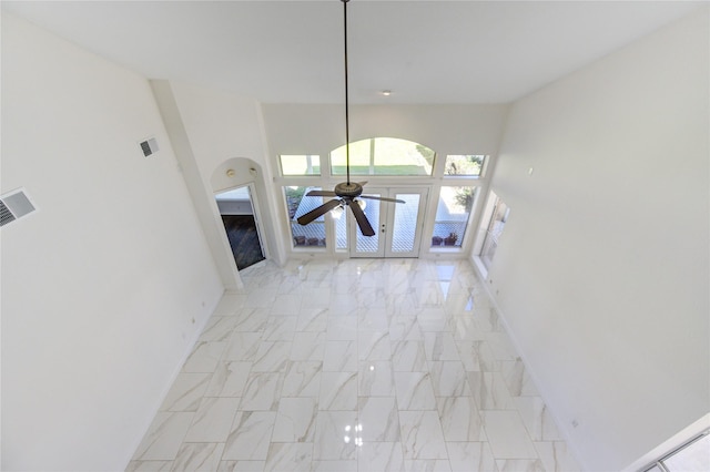 unfurnished living room with marble finish floor, baseboards, ceiling fan, and a towering ceiling