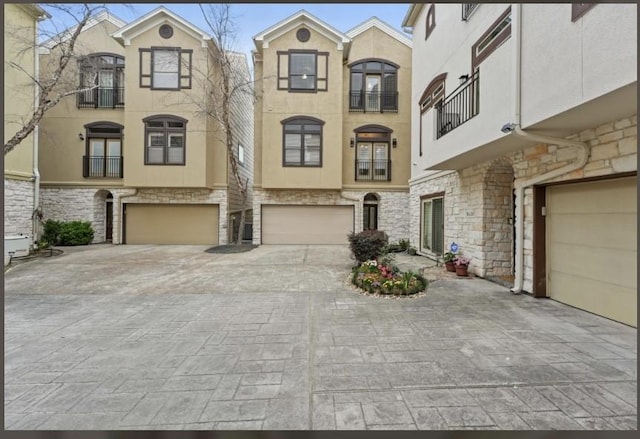 view of front of home featuring decorative driveway, stone siding, a garage, and stucco siding