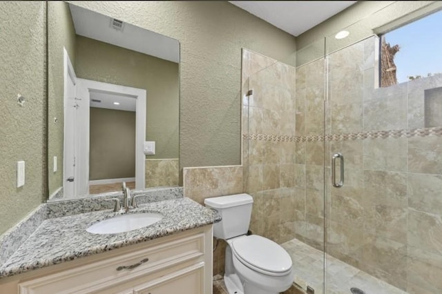 full bath featuring visible vents, toilet, a stall shower, vanity, and a textured wall