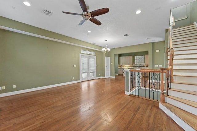 unfurnished living room featuring visible vents, ceiling fan with notable chandelier, wood finished floors, stairway, and baseboards