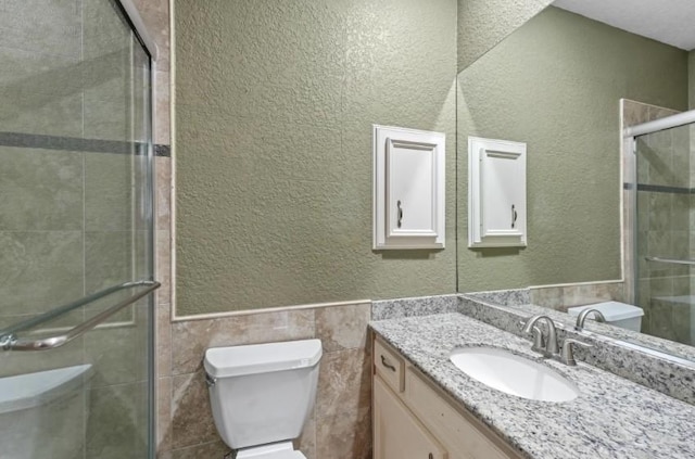 bathroom with vanity, a shower stall, tile walls, toilet, and a textured wall