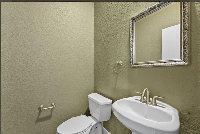 bathroom with toilet, a textured wall, and a sink