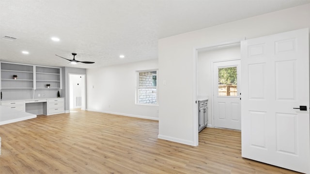 unfurnished living room featuring a wealth of natural light, visible vents, light wood-style floors, and a ceiling fan