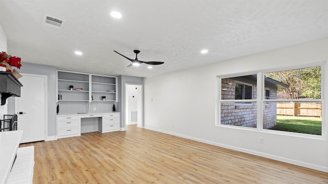 unfurnished office with visible vents, ceiling fan, light wood-type flooring, built in desk, and a textured ceiling