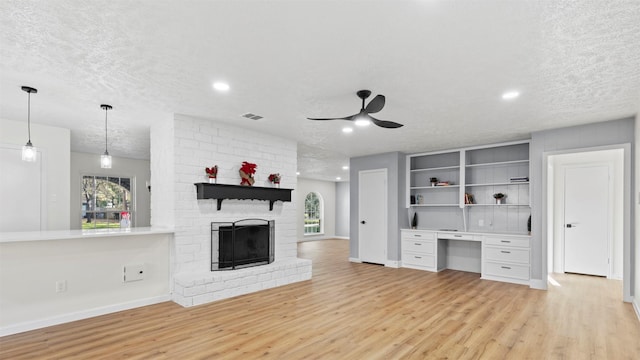 unfurnished living room featuring ceiling fan, a fireplace, light wood finished floors, and a textured ceiling