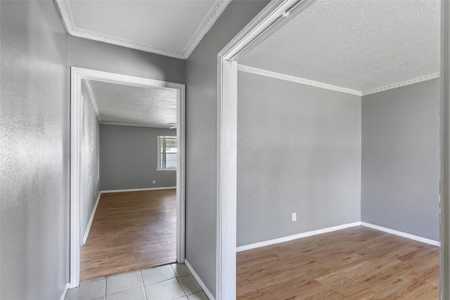 corridor featuring a textured ceiling, wood finished floors, baseboards, and ornamental molding