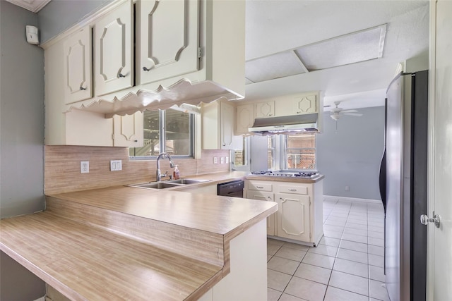 kitchen featuring under cabinet range hood, a sink, backsplash, a peninsula, and light tile patterned flooring