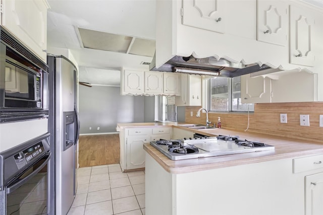 kitchen with black appliances, a sink, a peninsula, light countertops, and light tile patterned floors