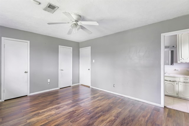 unfurnished bedroom featuring multiple closets, wood finished floors, visible vents, and baseboards