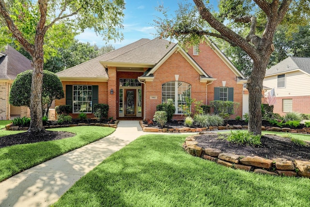 traditional home featuring a front yard, brick siding, and roof with shingles