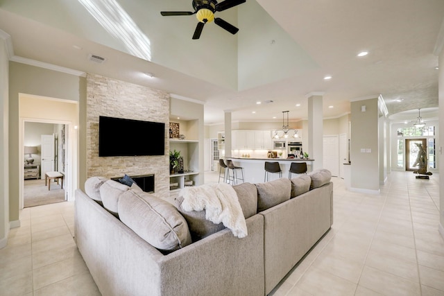 living room with visible vents, a stone fireplace, ceiling fan, and ornamental molding