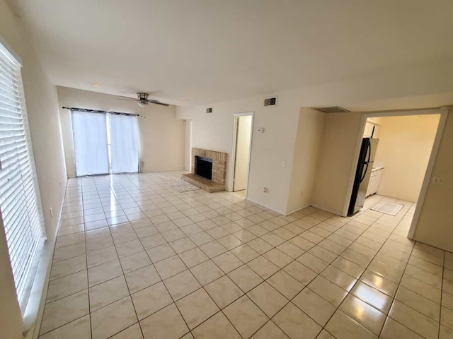 unfurnished living room featuring light tile patterned floors, visible vents, a brick fireplace, and ceiling fan