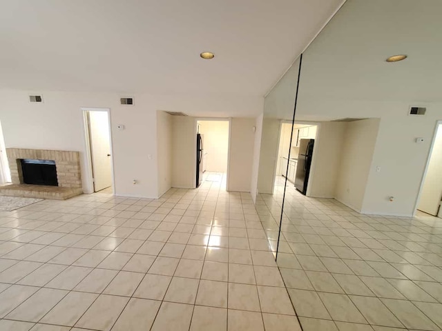 unfurnished room featuring light tile patterned floors, visible vents, and a brick fireplace