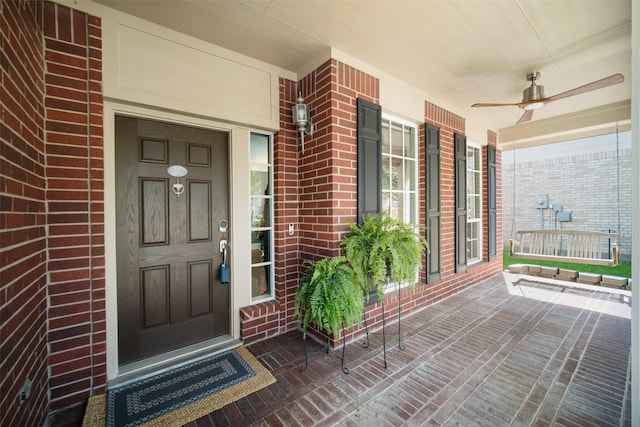 entrance to property with brick siding, a porch, and a ceiling fan