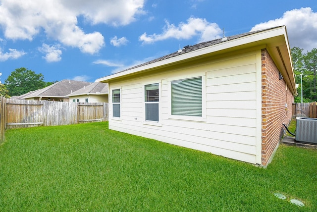 rear view of house with a yard, a fenced backyard, brick siding, and central AC