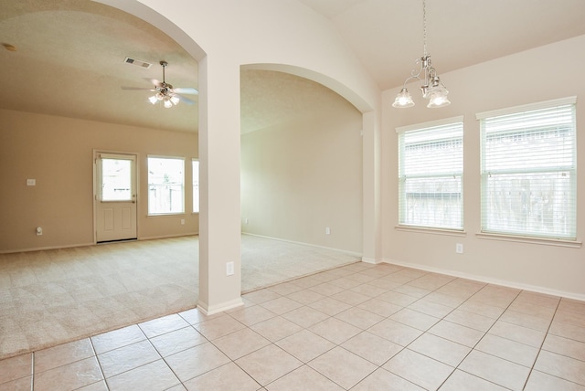 unfurnished room featuring ceiling fan with notable chandelier, arched walkways, light tile patterned floors, light colored carpet, and vaulted ceiling