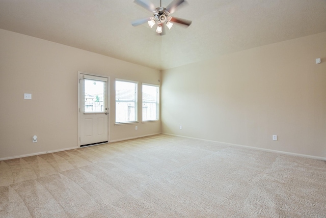 empty room featuring light carpet, baseboards, ceiling fan, and vaulted ceiling