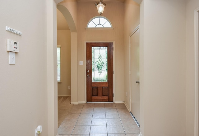 foyer featuring light tile patterned floors, baseboards, and arched walkways