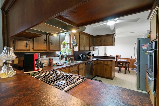 kitchen with a sink, dark countertops, appliances with stainless steel finishes, a peninsula, and ceiling fan