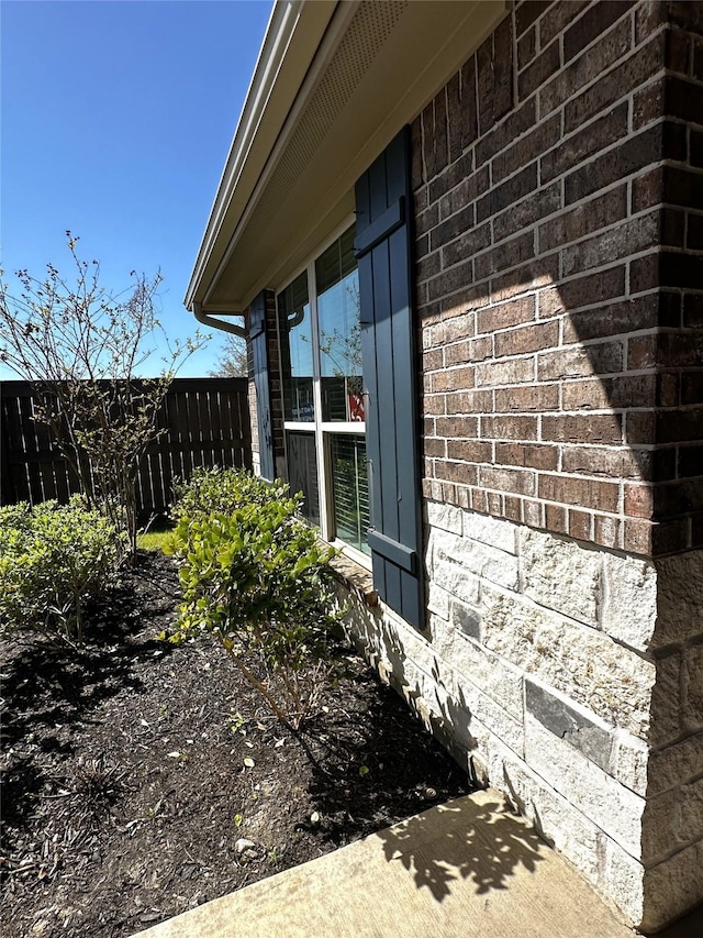 view of side of home featuring brick siding and fence