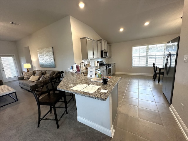 kitchen featuring visible vents, a breakfast bar, vaulted ceiling, light tile patterned flooring, and stainless steel appliances